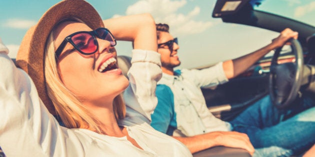 Side view of joyful young woman relaxing on the front seat while her boyfriend sitting near and driving their convertible