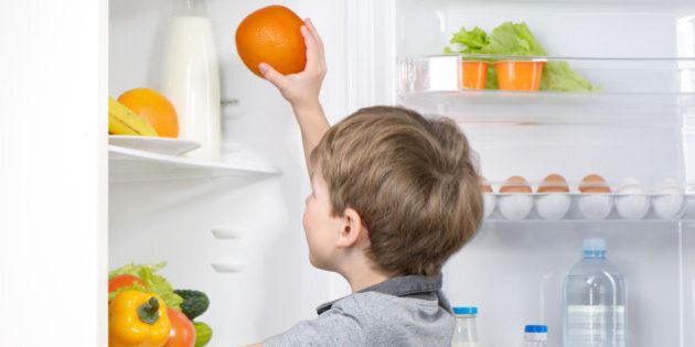 Little cute boy picking orange from fridge. Vegetables and fruits in the refrigerator