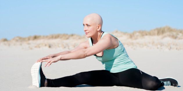 Young beautiful woman is stretching on the beach after enduring chemotherapy because of cancer.
