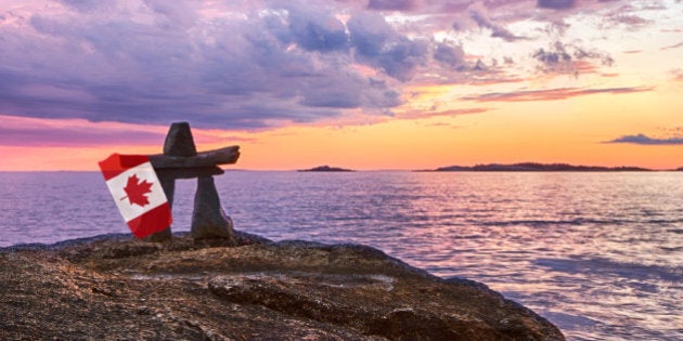 An Inukshuk at sunset holding a Canadian flag overlooking a body of water.