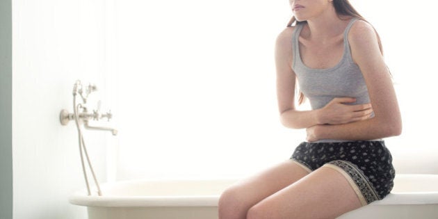 Woman sitting on edge of bathtub holding stomach