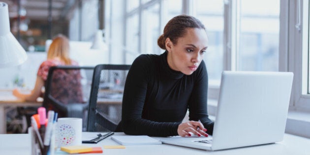 Image of woman using laptop while sitting at her desk. Young african american businesswoman sitting in the office and working on laptop.