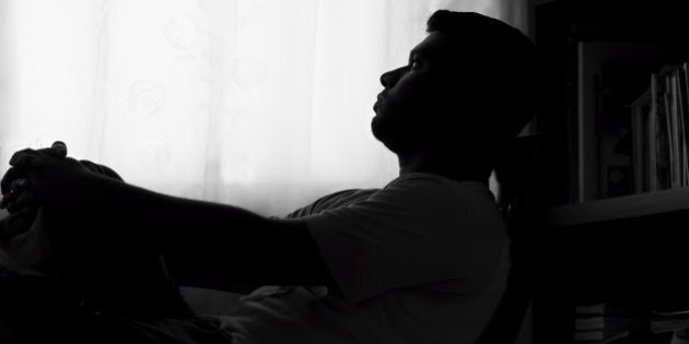 Silhouette of a sad man sitting in front of the bookshelf. Looking towards the curtained window.