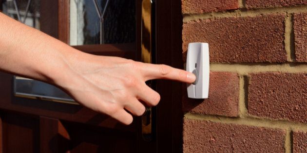 Woman extends her hand to ring a doorbell at the front door of a house