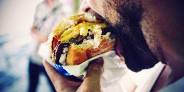 Close-Up Of Man Eating Cheeseburger On Street