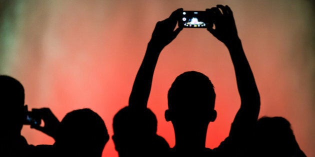 Black silhouettes of people taking pictures with smartphone at dark night in Barcelona city with only illuminated by the light of the Font Magica show with the colors and the contrast.