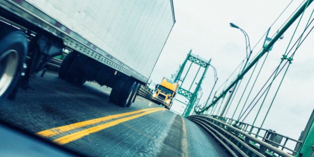 Driving in a speeding car passing two large oncoming semi tractor trailer trucks at the apex of the Thousand Islands Bridge - a very tall and extremely narrow suspension bridge along the US Interstate Route 81 expressway. This bridge crosses the Saint Lawrence River in the Thousand Islands Region along the international border between Ontario, Canada and New York State, USA.