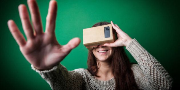 Color shot of a young woman looking through a cardboard, a device with which one can experience virtual reality on a mobile phone.