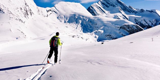 Backcountry skier skinning along a gradual snow slope towards radical looking mountains in Burstall Pass.