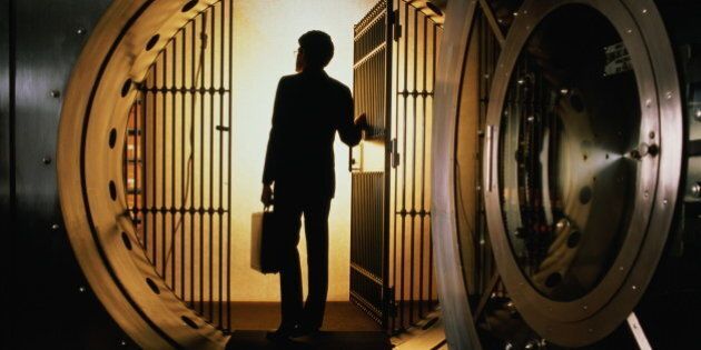 Man with briefcase silhouetted in open door of bank vault