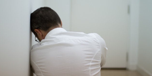 Man in white corridor in front of door, he looks tired/depressed/pensive.