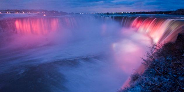 Niagra Falls is lit up at night as seen from Canada.