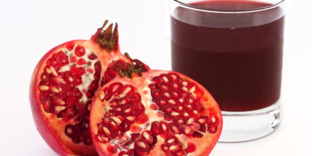Glass of fresh pomegranate juice with ripe pomegranate cut into two halves, on a white background.