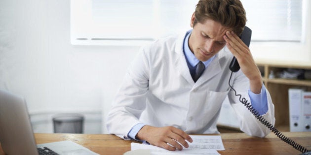 Shot of a concerned doctor sitting in his office and talking on the phone while looking over paperwork