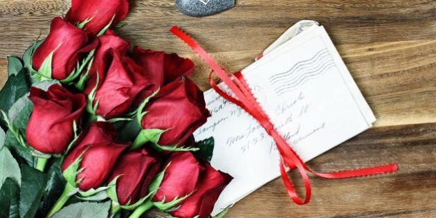 Long stem red roses with a stack of old letters tied with a red ribbon and card a little stone heart with the word love.