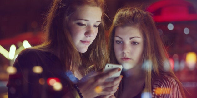 15 year old girl's face lit up by an iPhone at a bus stop