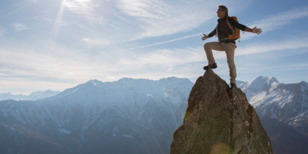 Hiker stands on pinnacle summit, arms outstretched