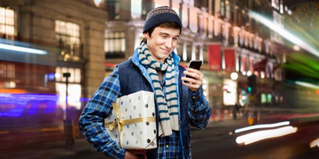 man holding shopping looks at mobilephone in city.