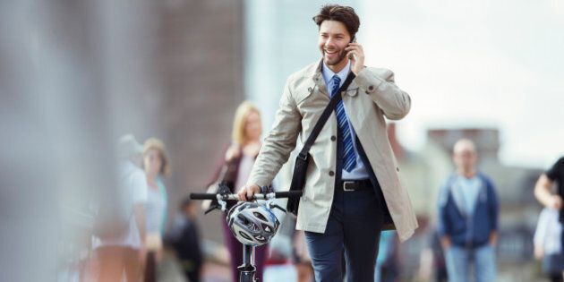Businessman talking on cell phone pushing bicycle in city