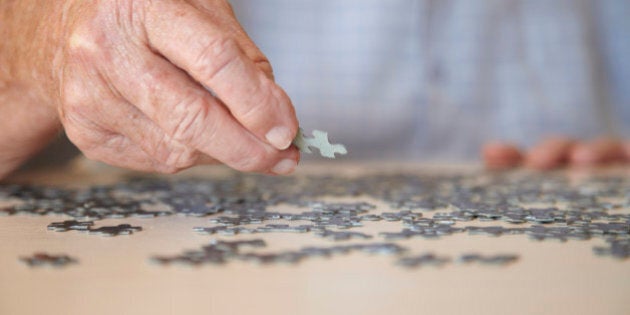 Elderly man, aged 77, looking for pieces of a jigsaw puzzle in a private retirement home