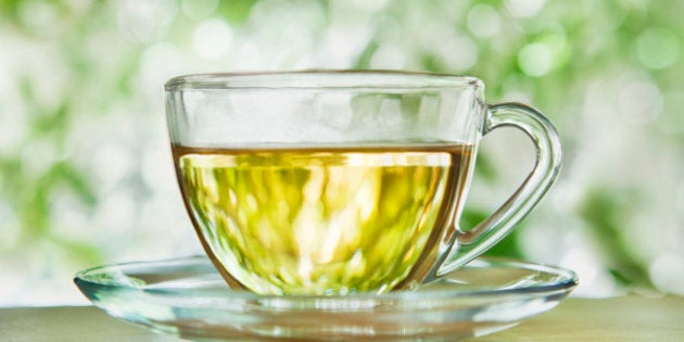 A glass cup and saucer with herbal tea against blurred foliage outdoors.