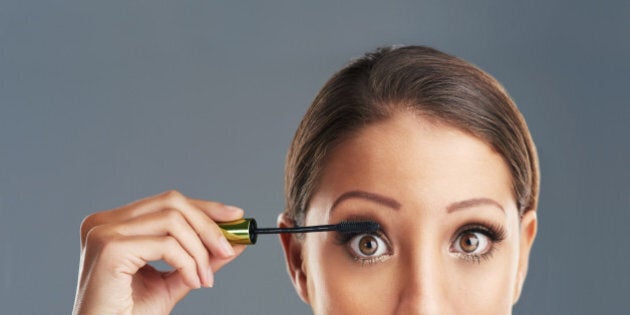 Studio portrait of a beautiful young woman putting on mascara against a grey background