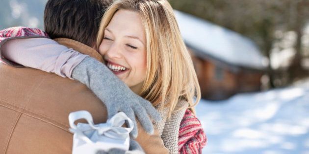 Smiling woman holding Christmas gift and hugging man in snowy field