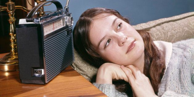 1960s TEENAGE GIRL LYING ON COUCH LISTENING TO MUSIC ON PORTABLE BATTERY POWERED RADIO (Photo by H. Armstrong Roberts/ClassicStock/Getty Images)