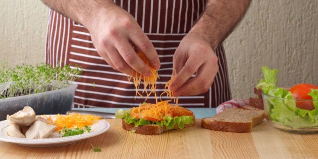 Man cooking big sandwich in home kitchen on a wooden table