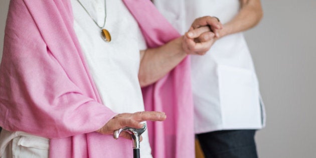 Senior woman with a crutch getting support from nurse. Lower section.