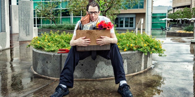 Photo of an out-of-work businessman, sitting outside his office building with his box of meager belongings as he gets rained on. 'When it rains, it pours.'