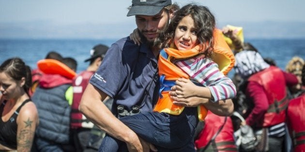 LESBOS ISLAND, GREECE - SEPTEMBER 19: A volunteer carries a refugee girl upon her arrival on the shore of Eftalou beach, north of the port city of Mytilini after crossing the Aegean sea from Turkey on September 19, 2015 in Lesbos Island, Greece. (Photo by Ozge Elif Kizil/Anadolu Agency/Getty Images)