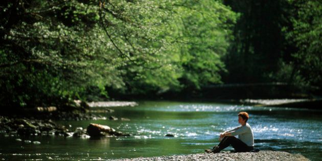 Woman sitting on gravel bar with a river flowing by, Carmanah Walbran Provincial Park, Vancouver Island, British Columbia, Canada.