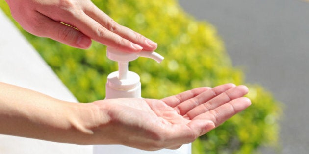 Female using gel sanitizer with green healthy blurry background.