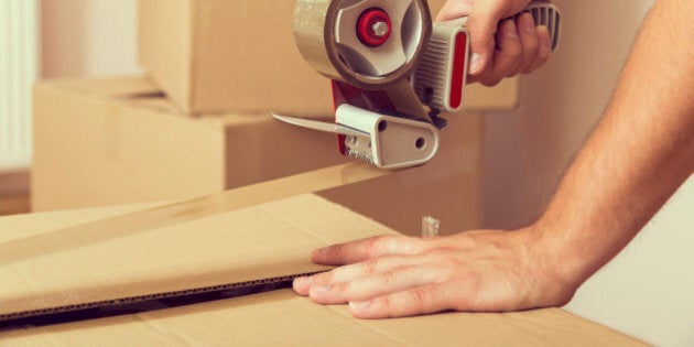 Close up of a guy's hands holding packing machine and sealing cardboard boxes with duct tape