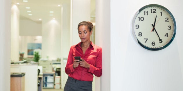 Businesswoman in office using PDA near a clock