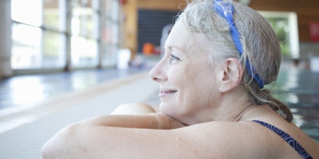 Senior baby boomer woman resting on edge of swimming pool, enjoying a quite moment