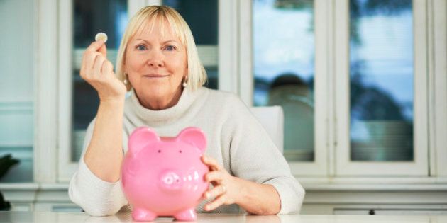 portrait of happy caucasian senior woman saving euro coin into piggybank and smiling at camera