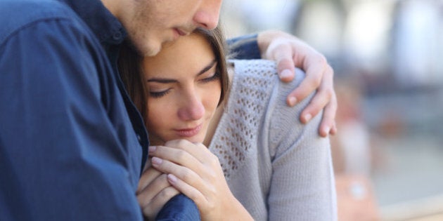 Man comforting his sad mourning friend embracing her in a park