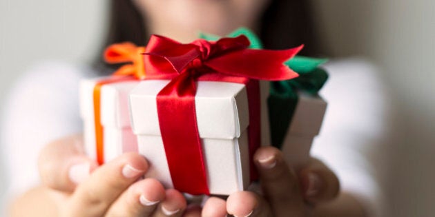 Woman holding a small gift box in a gesture of giving. Christmas holiday or special occasion gift box with red, green and orange ribbon.