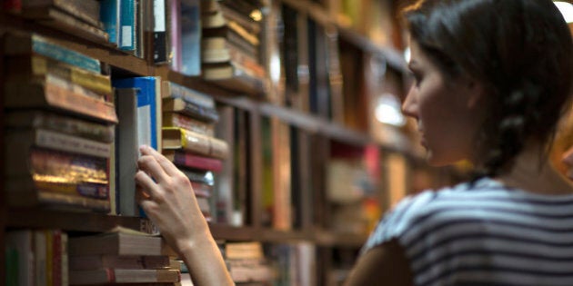 Beautiful woman looking at books in a library. Ambient light to emphasize the mood and location. Converted from RAW.