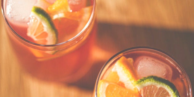 Top down view of 2 glasses of fruity punch with ice cubes and slices of lime and orange.