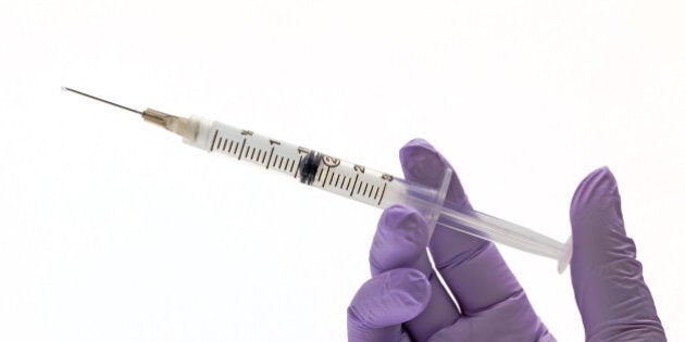 A human hand wearing protective glove holding a filled syringe needle.