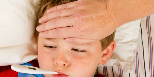 Sick child boy being checked for fever and illness while resting in bed