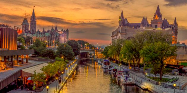 A summer evening in downtown Ottawa. This is the Rideau canal shot from the MacKenzie King Bridge.On the left is the Canadian Parliament buildings, on the right the Chateau Laurier hotel.People are strolling along the walk and pleasure craft gently bob in their moorings along the canal.