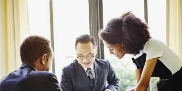 Businesswoman standing at end of table in restaurant presenting document on digital tablet to businessmen