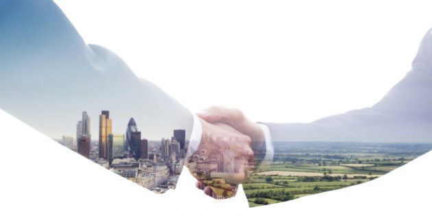 A double exposure of two business men shaking hands with a view of the City of London and of a green fields landscape.