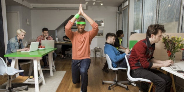 Young man exercising while colleagues work