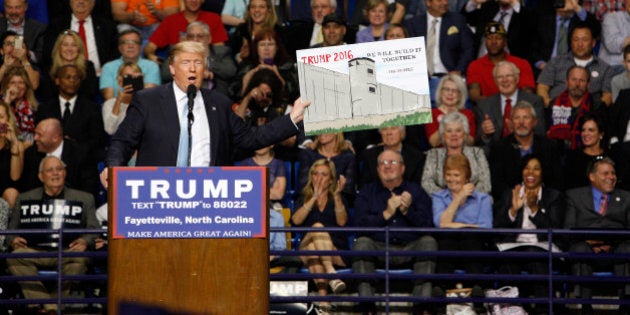 U.S. Republican presidential candidate Donald Trump holds a sign supporting his plan to build a wall between the United States and Mexico that he borrowed from a member of the audience at his campaign rally in Fayetteville, North Carolina March 9, 2016. Trump was interrupted repeatedly by demonstrators during his rally. REUTERS/Jonathan Drake