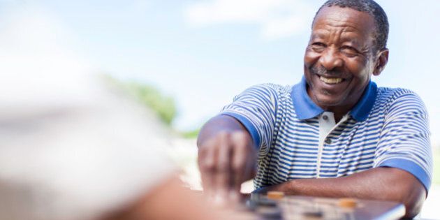 African male senior smiling, playing a game of chess against his friend in Langebaan, Western Cape, South Africa.